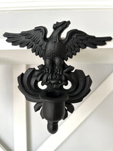A black metal double eagle wall sconce mounted on a white painted wooden wall or shelf.