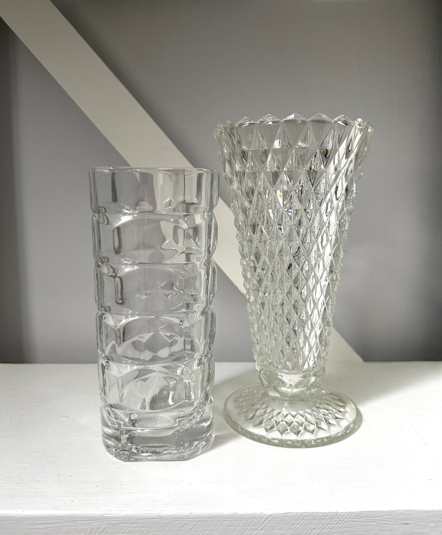 Two clear glass vases on a white surface with a gray background
