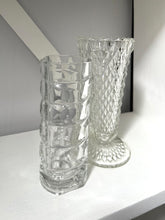Two clear glass vases on a white surface with a gray background