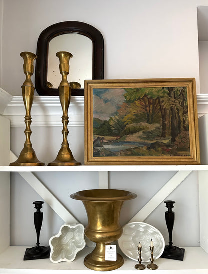 Decorative items including brass and black candlesticks, a mirror, and a framed painting on a white shelf.