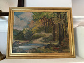 Framed painting of a landscape with trees and a body of water on a white surface.