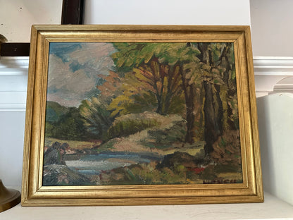 Framed painting of a landscape with trees and a body of water on a white surface.