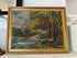 Framed painting of a landscape with trees and a body of water on a white surface.