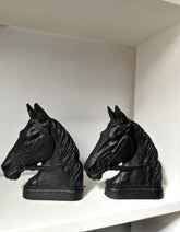 A pair of black horse head bookends displayed on a white shelf against a white wall.