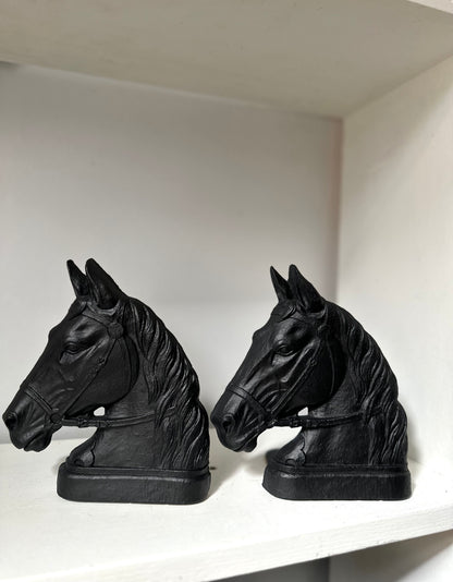 A pair of black horse head bookends displayed on a white shelf against a white wall.