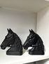 A pair of black horse head bookends displayed on a white shelf against a white wall.