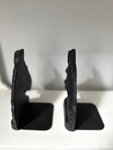A pair of black rustic stone bookends with a carved mountain or cliff face design, standing on a white surface against a light gray background.