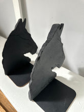 Two black horse head bookends standing on a white shelf against a light gray wall.