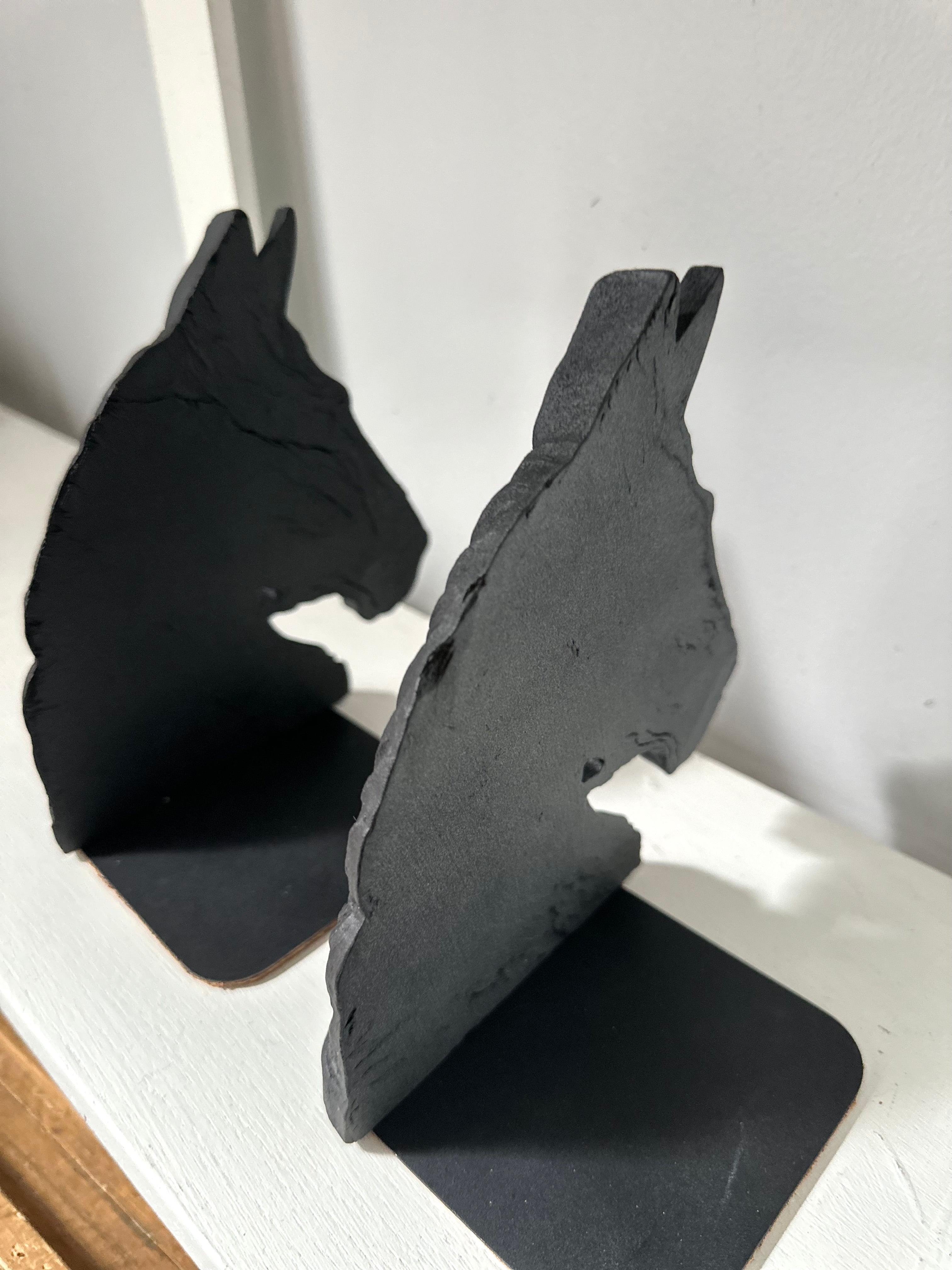 Two black horse head bookends standing on a white shelf against a light gray wall.
