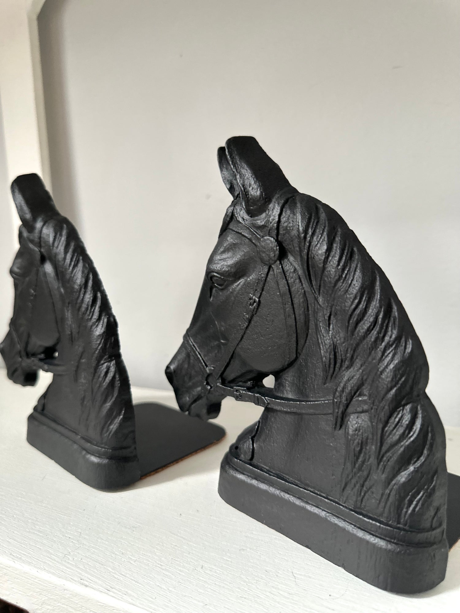 A pair of black horse head bookends displayed on a white shelf against a light gray background.