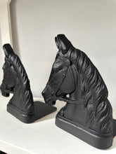 A pair of black horse head bookends displayed on a white shelf against a light gray background.