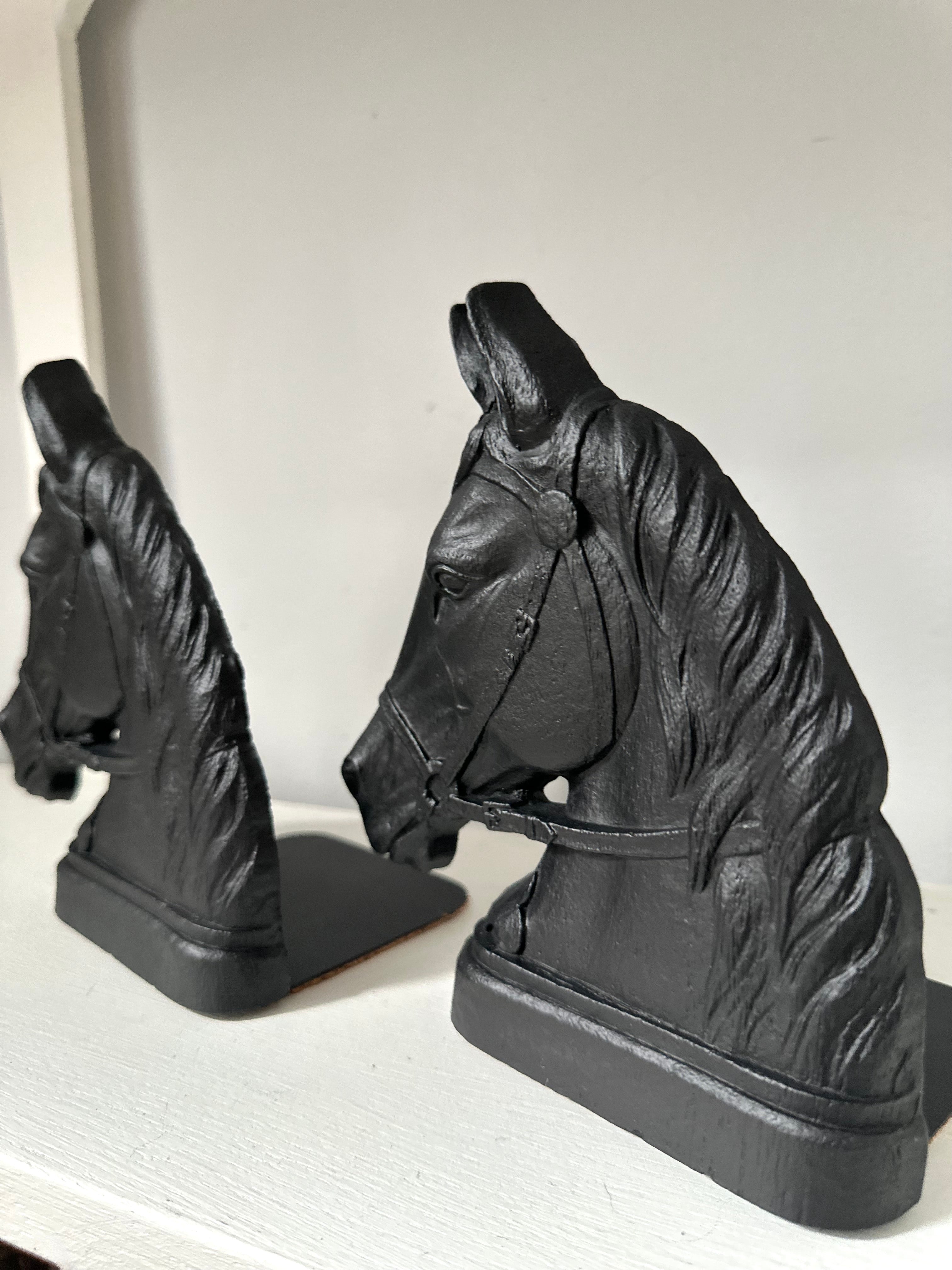 A pair of black horse head bookends displayed on a white shelf against a light gray background.