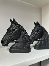 Two black horse head bookends displayed on a white shelf against a light gray background.