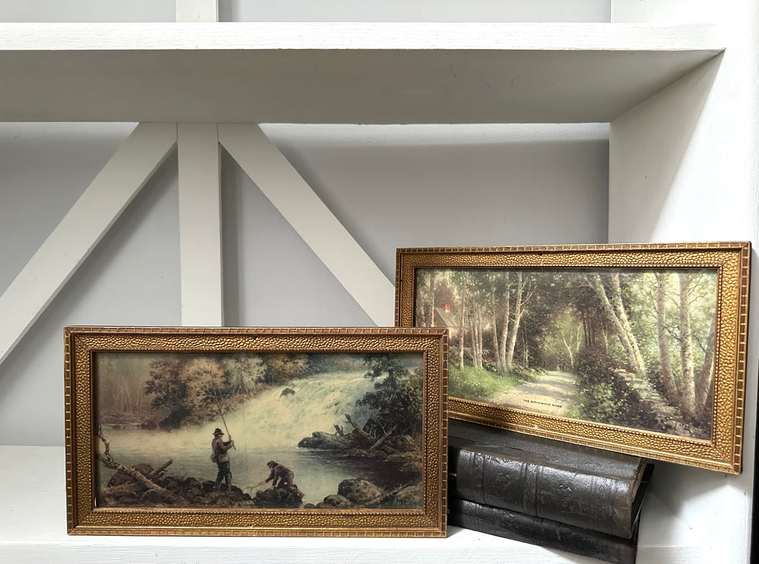 Two framed paintings on a shelf against a white wall