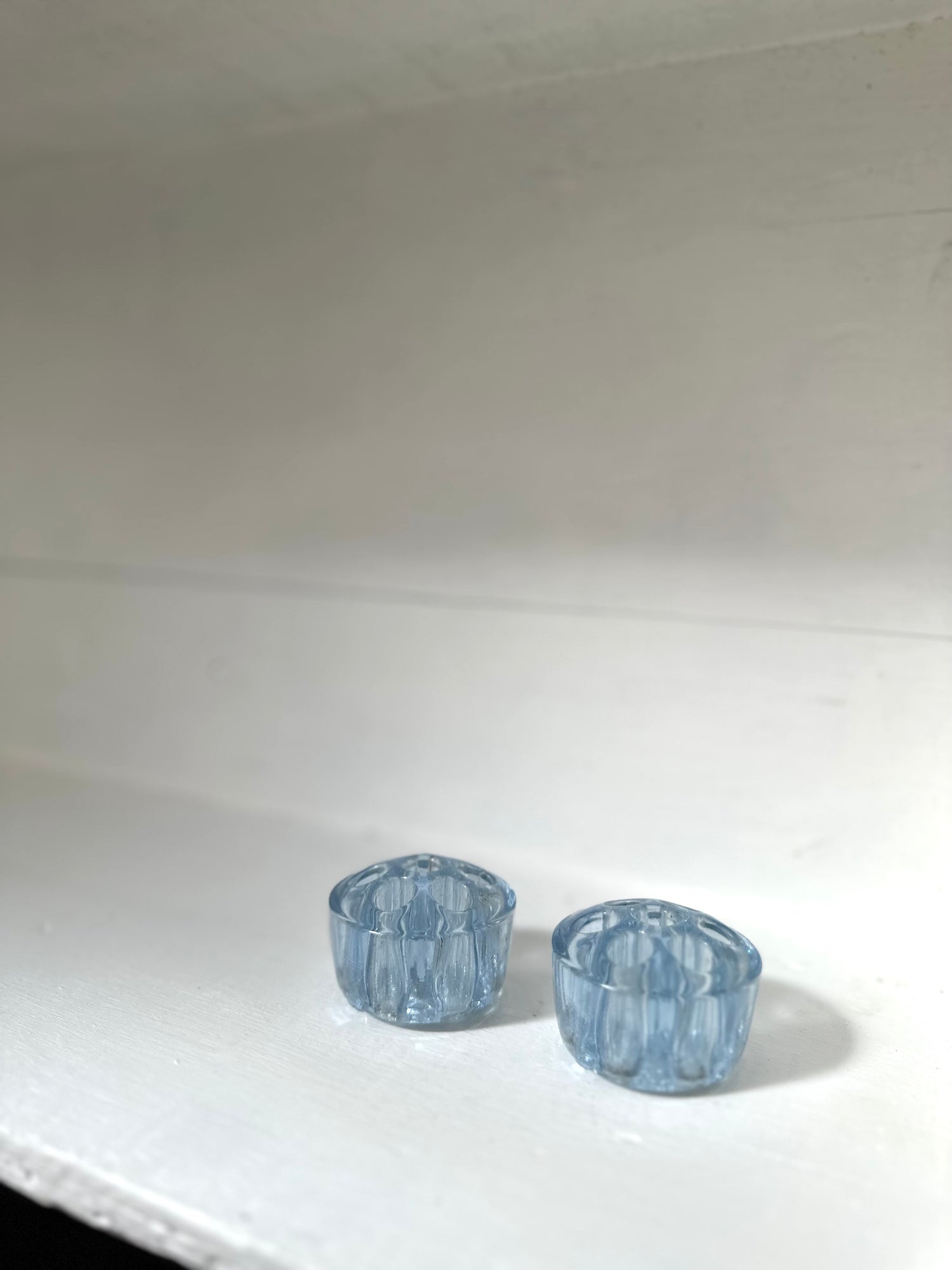 Two small light blue faceted glass cups or candle holders on a white surface against a white background.