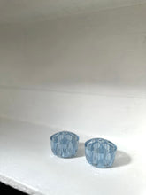 Two small light blue faceted glass cups or candle holders on a white surface against a white background.
