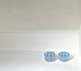 Two small light blue faceted glass cups or candle holders placed side by side on a white surface against a white background.
