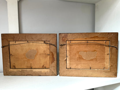 Two vintage wooden picture frames shown from the back, resting on a white shelf against a plain gray wall.