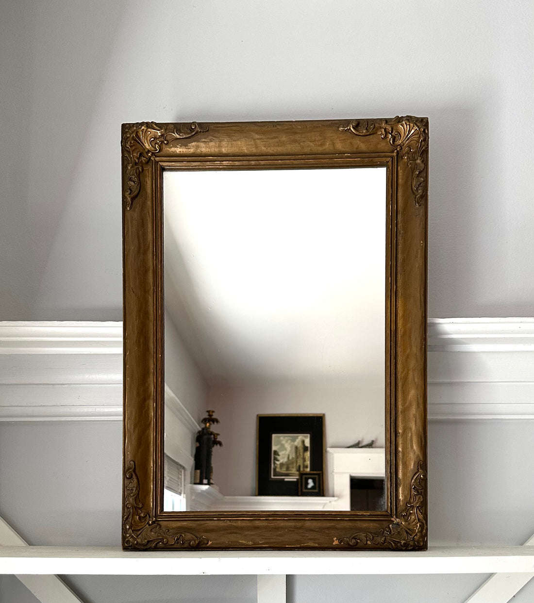 Decorative gold-framed mirror on a white wall