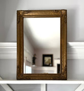 Decorative gold-framed mirror on a white surface with a blurred background