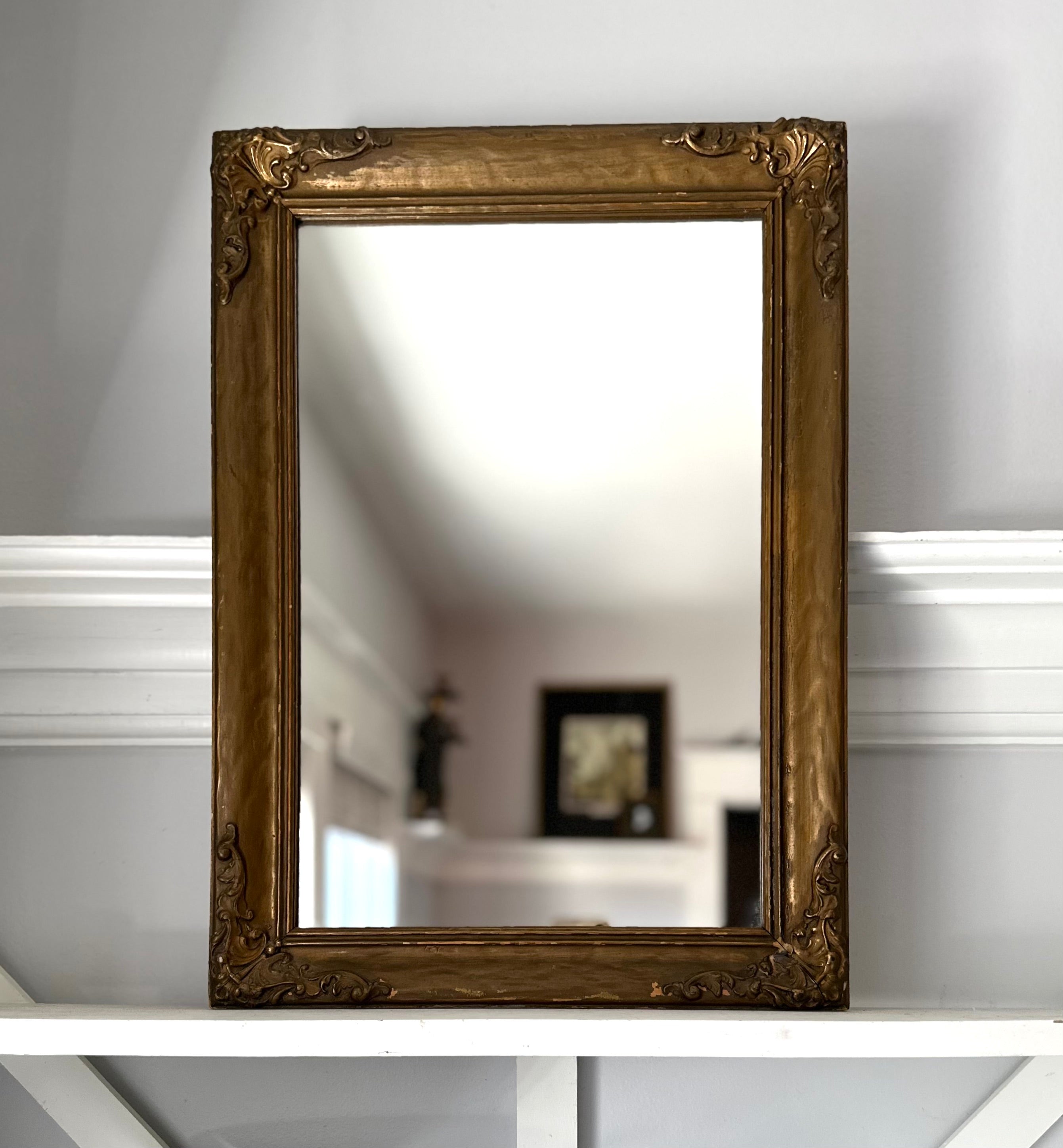 Decorative gold-framed mirror on a white surface with a blurred background