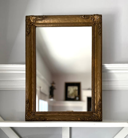 Decorative gold-framed mirror on a white surface with a blurred background