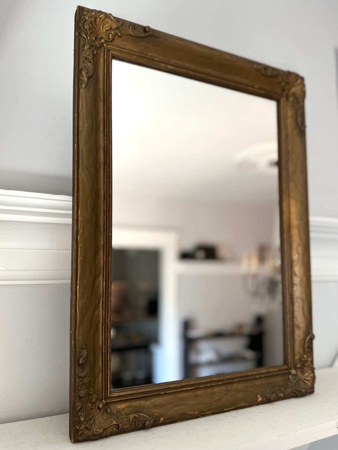 Decorative gold-framed mirror on a white surface with a blurred indoor background