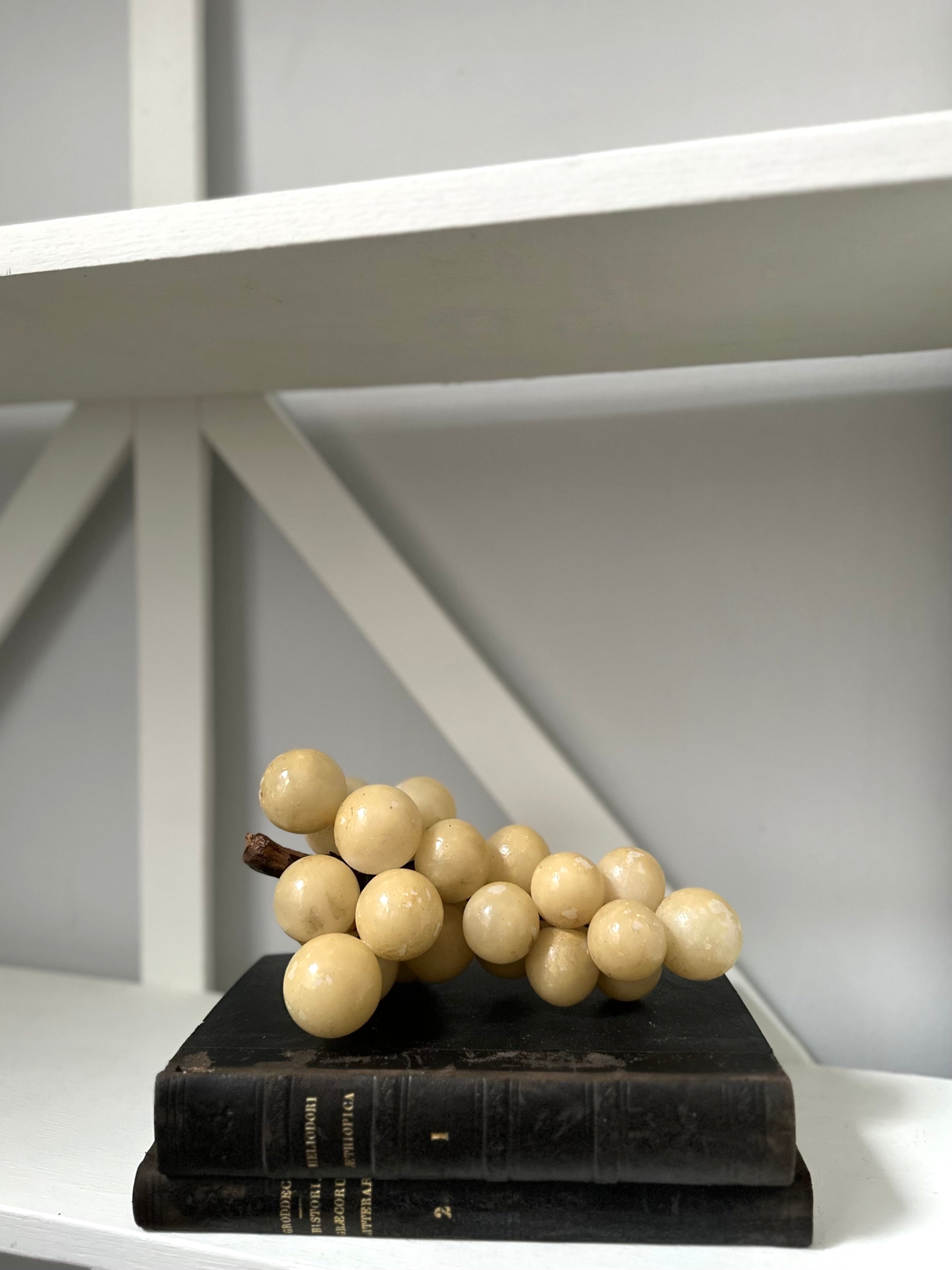 Decorative sculpture of grapes on a stack of books against a white background