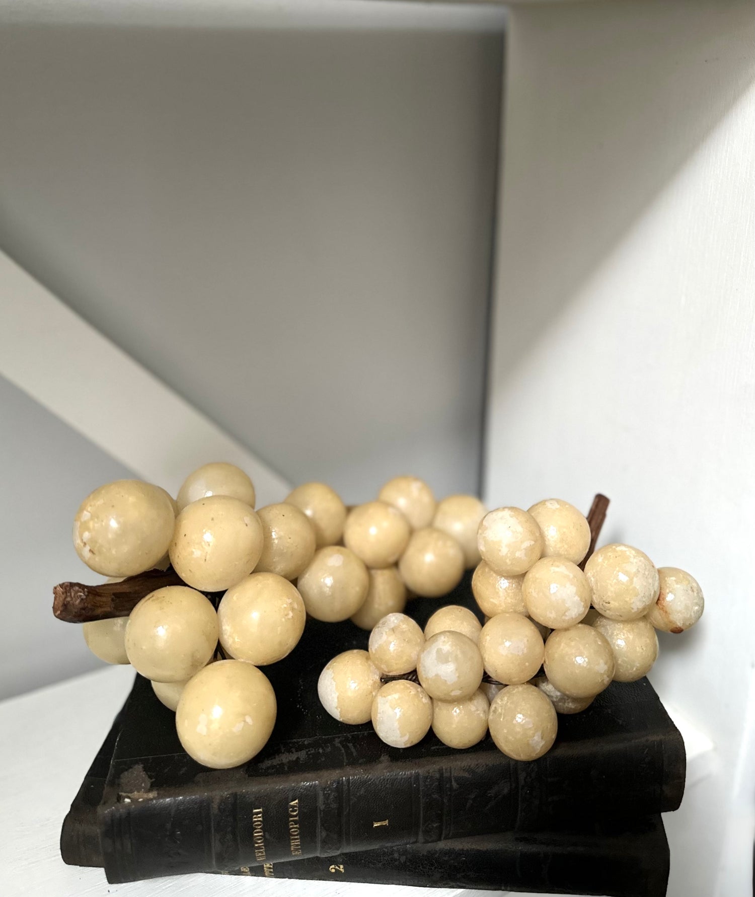 Decorative faux white grapes on a black stand against a neutral background
