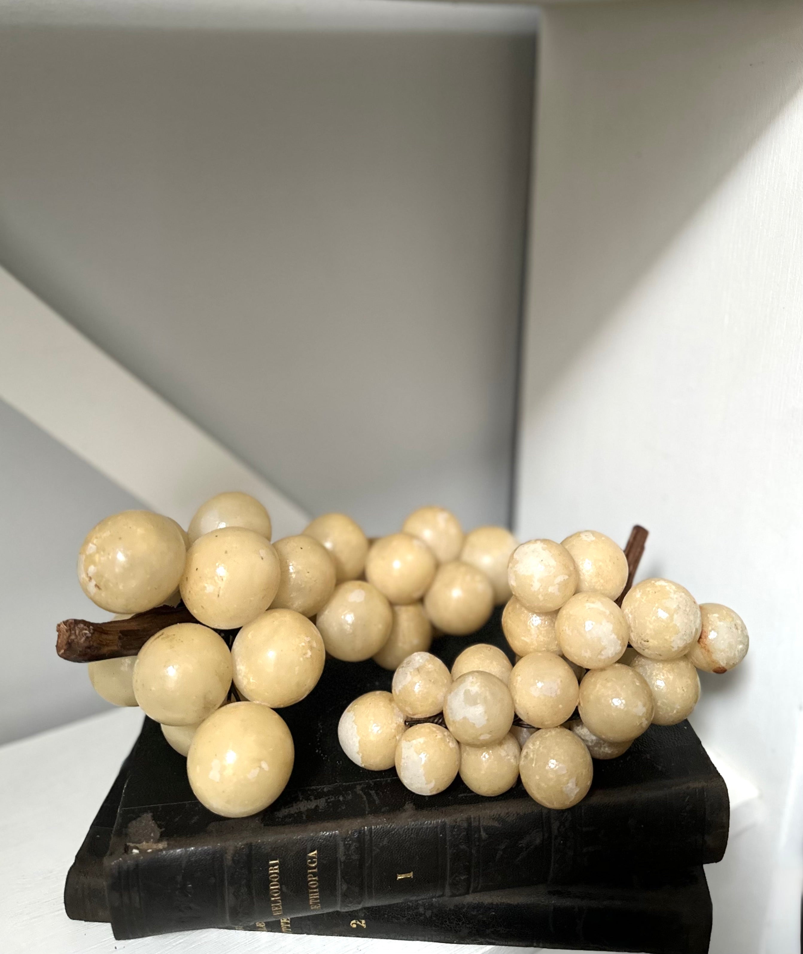 Decorative faux white grapes on a black stand against a neutral background