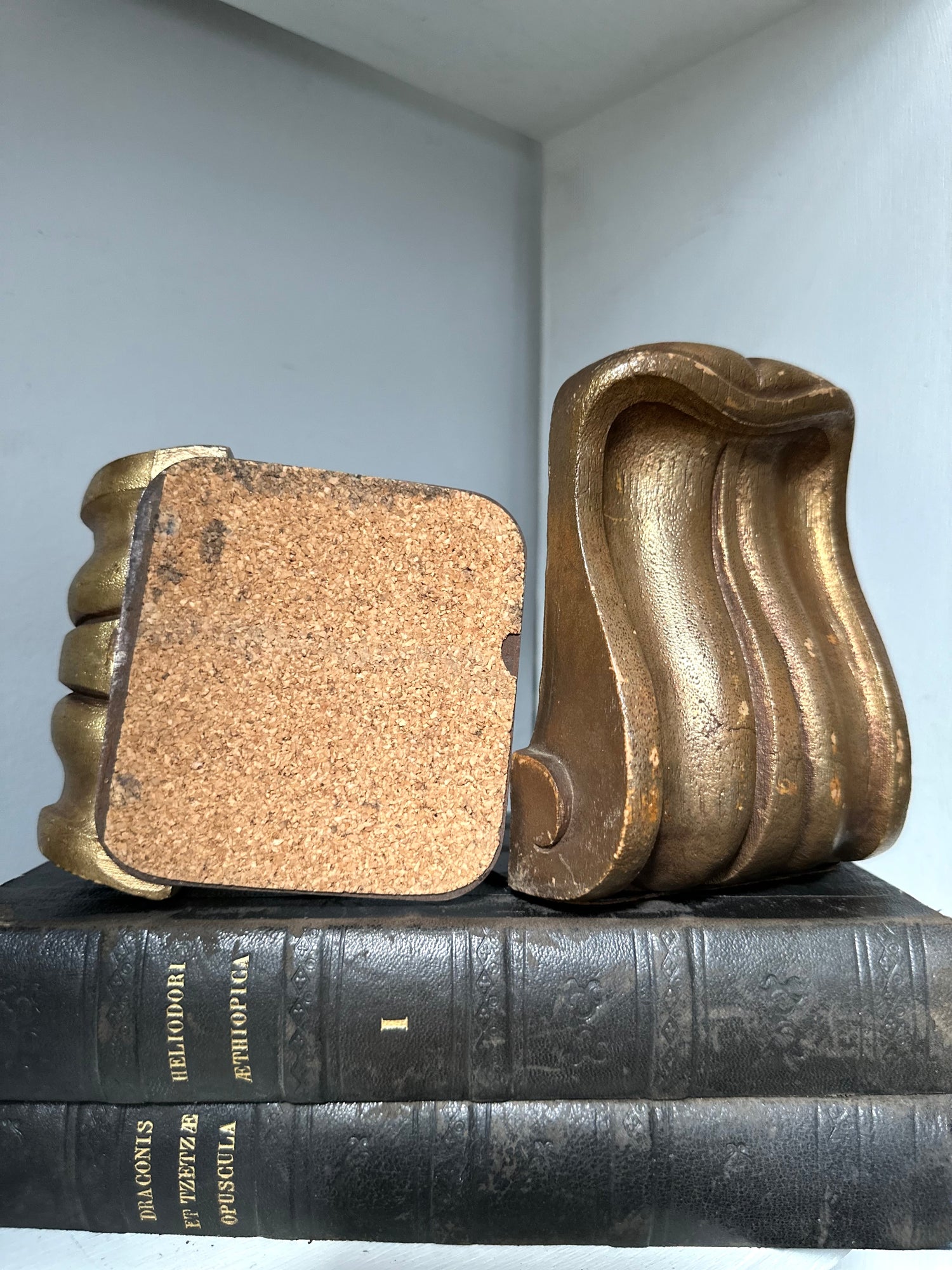 Decorative gold bookends on a stack of books with a light gray wall background