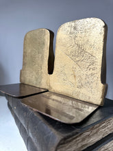 Two metallic bookends on a reflective surface with a neutral background